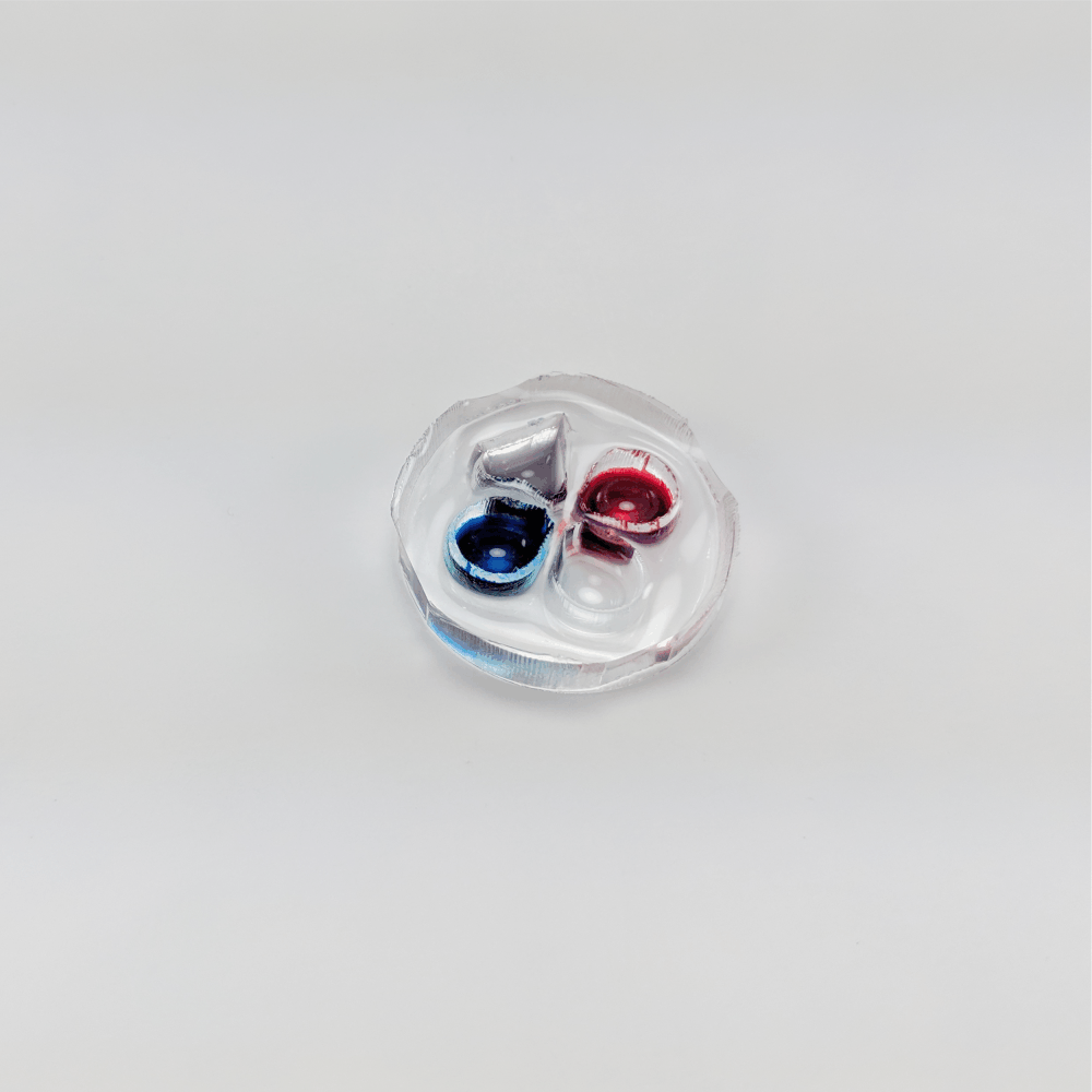 Photograph of eNUVIO's OMEGA AG device with three chambers. Source chamber 1 is filled with blue liquid, source chamber two is filled with red liquid, neuronal chamber is filled with colorless liquid, waste chamber is filled with silver liquid.